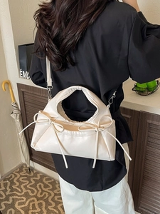 Cream white crossbody bag with bow details and soft pleats shown on a model