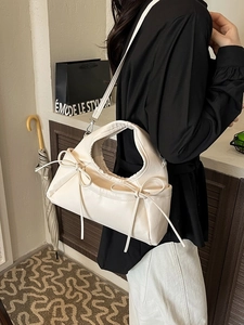 Creamy white pleated crescent bag with delicate bow accents shown in a stylish outfit