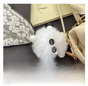 Detail of white plush pendant charm with sunglasses and gold chain on beige handbag