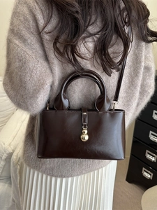 Vintage dark coffee leather tote bag with gold charm on a warm brown sweater background