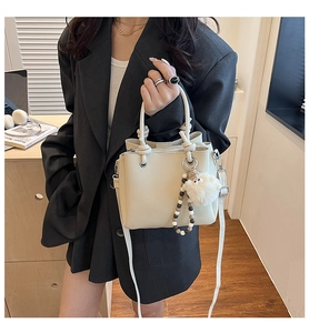 Detail view of a beige lychee pattern bucket bag with sheep plush charm and knot handle