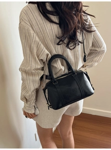 Detail shot of a black textured Boston bag with golden hardware on a female model