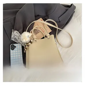 Close-up of beige lychee grain bucket bag with plush sheep charm on white fabric