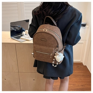 Détail du sac à dos vintage en cuir mat marron avec un pendentif d'agneau en peluche blanc