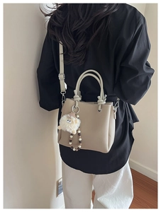 Detail of beige lychee textured tote bag with cute white sheep charm and pearl strap