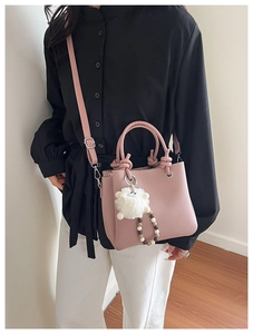 Detailed view of a pink crossbody tote bag with a plush charm on a model's arm