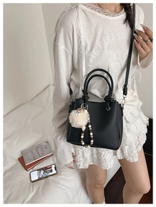 Detail of black pebbled leather handbag with round handles and plush lamb charm