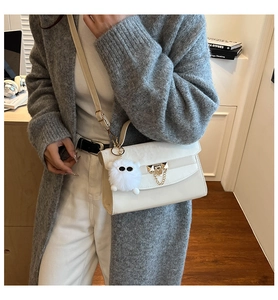 Detail van een crèmewitte crossbodytas met gouden ketting en pluche bal op model