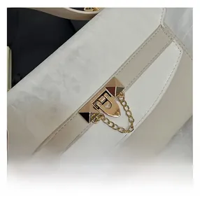 Detail van wit-beige crossbodytas met gouden gesp en metalen kettingschakels