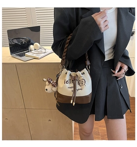 Detail of canvas bucket bag with drawstring closure, woven handle and plush dog charm