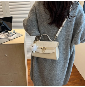 Beige lederen crossbodytas met goudkleurig slot en pluche hanger getoond op model