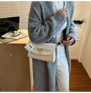 Detail van beige lederen crossbodytas met gouden kettinggesp en witte pompon hanger