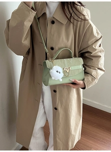 Detail van lichtgroene crossbodytas met goudkleurig slot, ketting en witte pompon hanger