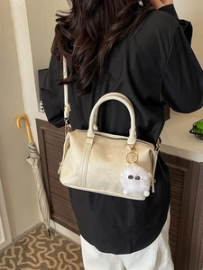 Chic off-white Boston bag with pleated texture and plush charm in a home setting