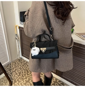 Detail van zwarte crossbodytas met gouden sluiting en witte pluche kattenbedeltje