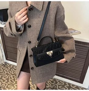 Detail van zwarte crossbodytas met geplooide flap en gouden kettingsluiting