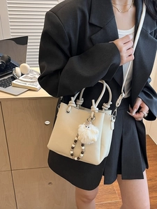 Off-white lychee grain tote bag with plush charm shown in a professional lifestyle setting