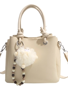 Chic beige tote bag with litchi texture and plush ball charm on white background
