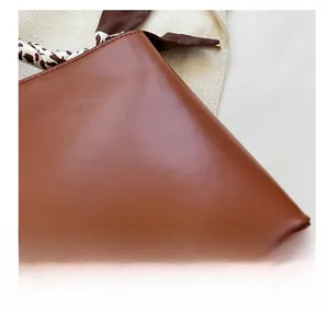 Détail macro du sac en similicuir marron avec un foulard décoratif en soie motif vache noir et blanc