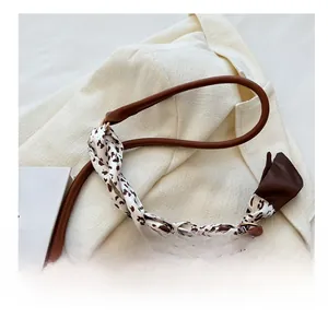 Détail d'un sac bandoulière en cuir marron avec un foulard en soie noué sur l'anse