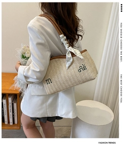 Détail d'un cabas en paille tissée avec broderie noire et foulard floral sur fond neutre