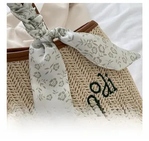 Detailed close-up of woven straw tote bag with floral silk scarf and green embroidery