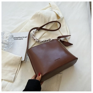 Détail du sac bandoulière en cuir marron avec un foulard en soie floral sur l'anse
