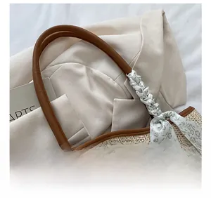 Close-up of hand-woven straw tote with leather strap and floral silk scarf detail