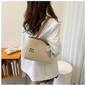 Detail of woven straw tote bag with embroidered 'm' and decorative floral silk scarf handle