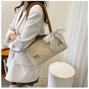 Detail of woven straw tote bag featuring leather straps and a floral silk ribbon bow