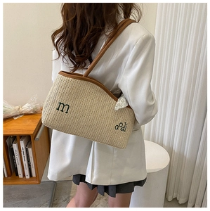 Détail d'un sac cabas en paille tissée avec anses brunes porté à l'épaule sur un blazer blanc