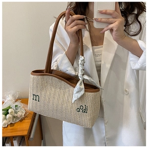 Détail d'un sac cabas en paille tressée avec poignées en cuir marron et foulard fleuri