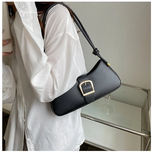 Close-up of black leather baguette bag featuring a large gold buckle and knotted handle detail