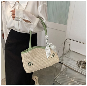 Détail d'un sac cabas en paille tissée avec bordure en cuir vert et foulard à fleurs