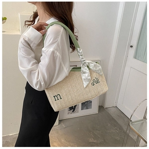 Detail of hand-woven straw tote bag with green handles and floral scarf decoration
