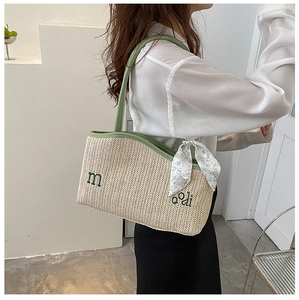 Detail of straw tote bag featuring green embroidery and floral scarf on shoulder strap