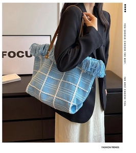 Close-up of blue and white woven tote bag featuring fringe details and leather straps