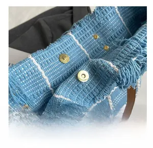 Detail of the magnetic gold buckle closure on a blue plaid tweed tote bag with tassels