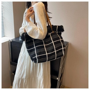 Detail shot of black and white checkered woven tote bag with fringe tassels and leather handles