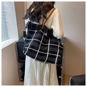 Detail view of large woven tote bag with black fringes and brown leather strap on model