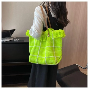Detail of neon green woven tote bag featuring white checkered pattern and long fringe trim