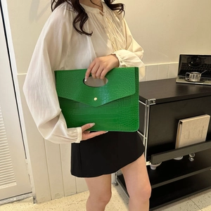 Dettaglio pochette a busta verde brillante con trama a coccodrillo e bottone dorato