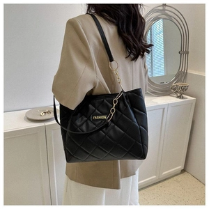 Detail of black quilted tote bag with gold chain strap worn on shoulder for daily use