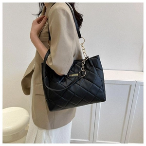 Detail of black quilted tote bag with gold chain strap and fashion label on the side