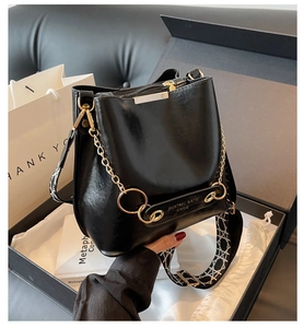 Close-up of black glossy bucket bag with gold chain and jacquard geometric strap