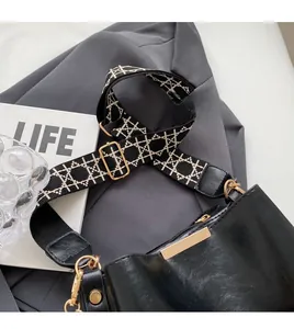 Detail of black leather bucket bag featuring a wide black and white checkered woven strap