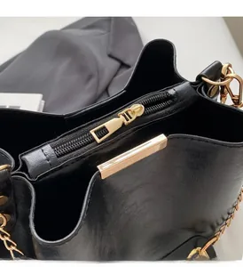 Detail of smooth gold zipper and metallic trim on a black faux leather bucket bag