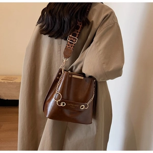 Detail of brown leather bucket bag with jacquard strap and gold chain accessories