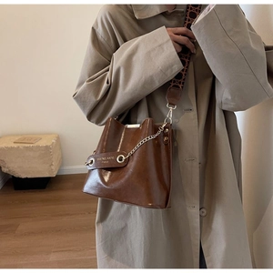 Detail of brown leather bucket bag featuring a metallic chain and vintage jacquard strap