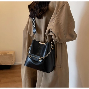 Detail of black bucket bag featuring gold chain and patterned wide woven strap